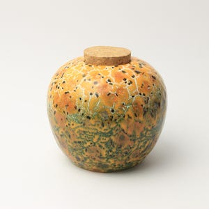 Könnte beinhalten: Ein rundes Keramikgefäß mit einem Korkstopfen. Die Oberfläche zeigt eine gesprenkelte Glasur mit einem Farbverlauf von warmem Gelb-Orange oben bis zu einem tiefen Waldgrün an der Basis, akzentuiert durch ein dunkles Rissmuster auf der Außenseite.