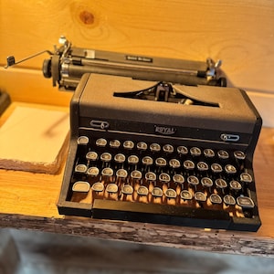 May include: A vintage black Royal typewriter with a metal body and a standard keyboard layout. The typewriter is sitting on a wooden surface.