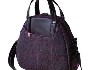 May include: A dark gray and burgundy plaid handbag with a brown leather handle and strap. The bag has a zipper closure and a small pocket on the front.