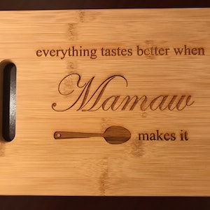 May include: A wooden cutting board with a handle, engraved with the text "everything tastes better when Mamaw makes it" and a spoon graphic.