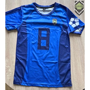 May include: A blue sports jersey featuring the number 8 in dark blue on the front. It has a crew neck and short sleeves. A crest is on the chest, and a white design is on the right sleeve. The jersey is likely for a sport.
