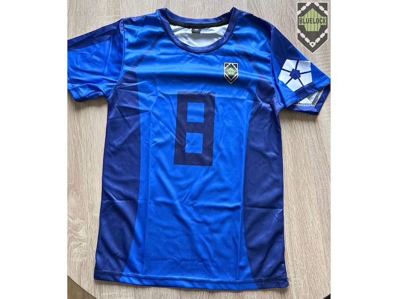 May include: A blue jersey with the number 8 in dark blue on the front. The jersey has a crew neck and short sleeves. A crest is on the chest, and a white design is on the right sleeve. The jersey is likely for sports.