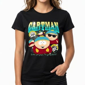 Op de afbeelding: Een zwart t-shirt met korte mouwen en een grafische print van het personage Cartman uit South Park. Het ontwerp bevat de tekst CARTMAN in grote blauwe en gele letters bovenaan en de zin Screw you guys, I'm going home! eronder.
