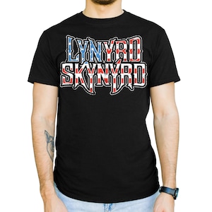 May include: Black t-shirt with the text "LYNYRD SKYNYRD" in a stylized font. The lettering is red, white, and blue, with a design inspired by the American flag. The shirt is short-sleeved and worn by a person.