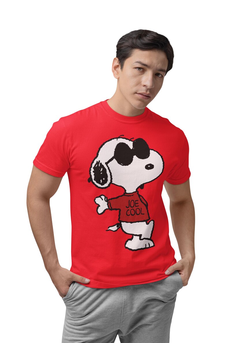 May include: A bright red short-sleeved t-shirt featuring a graphic print of the cartoon character Snoopy wearing black sunglasses and a red sweater with the text JOE COOL printed in black on the front of the sweater.