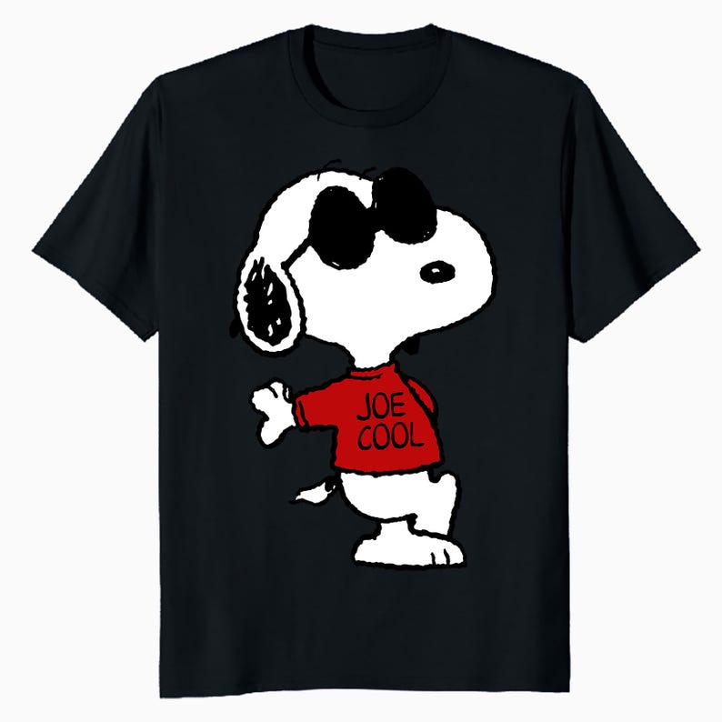 May include: A black short-sleeved t-shirt featuring a graphic of the cartoon character Snoopy wearing black sunglasses and a red shirt with the text JOE COOL printed in black. The character is depicted in a standing pose with one arm extended.