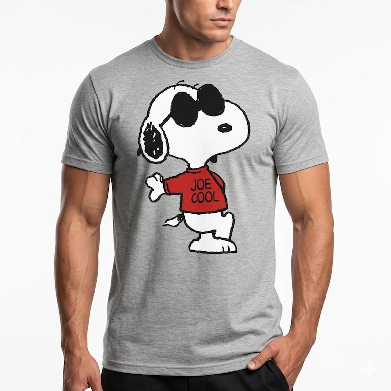 May include: A heather gray short-sleeved t-shirt featuring a graphic of the cartoon character Snoopy wearing black sunglasses and a red sweater with the text JOE COOL printed in black on the front of the sweater, centered on the chest area.