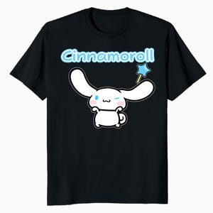 Pode incluir: Camiseta preta com o personagem Cinnamoroll. O personagem de desenho animado branco tem orelhas longas, uma expressão piscando e segura uma varinha de estrela azul. A palavra "Cinnamoroll" está escrita em azul claro acima do personagem.