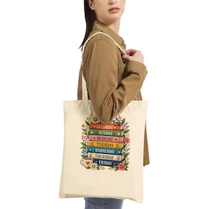 Op de afbeelding: Een crèmekleurige canvas tas met een kleurrijke afbeelding van een stapel van zeven boeken, elk gelabeld met een dag van de week van zaterdag tot vrijdag. De stapel is omringd door bloemillustraties en bevat een kleine koffiemok-icoon.