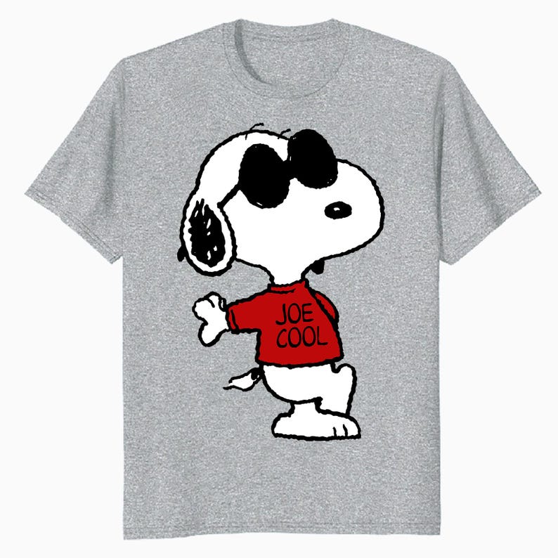 May include: A heather gray short-sleeve t-shirt featuring a graphic of the cartoon character Snoopy wearing black sunglasses and a red sweater with the text JOE COOL printed in black. The character is depicted in a standing pose.