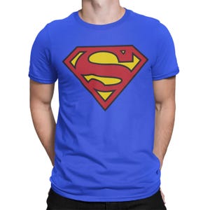 Op de afbeelding: Een felblauw T-shirt met korte mouwen en een groot, gecentreerd Superman-logo. Het embleem is een rode ruitvorm met een gele achtergrond en een opvallende rode letter S in het midden. Het shirt heeft een klassieke ronde hals en een rechte zoom.