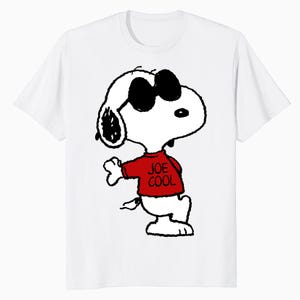 May include: A white short-sleeved t-shirt featuring a graphic of the cartoon character Snoopy wearing black sunglasses and a red shirt with the text JOE COOL printed in black. The character is depicted in a classic black and white line art style.
