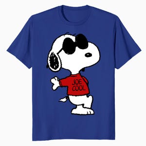 May include: A royal blue short-sleeved t-shirt featuring a graphic of the cartoon character Snoopy wearing black sunglasses and a red shirt with the text JOE COOL printed in black. The character is depicted in a standing pose with one arm raised.