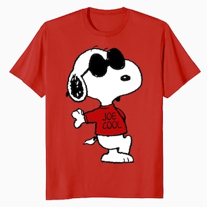 May include: A bright red short-sleeved t-shirt featuring a graphic of the cartoon character Snoopy wearing black sunglasses and a red shirt with the text JOE COOL printed in black. The character is white with black ears and outlines.