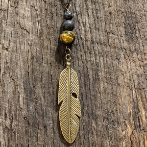 May include: A gold feather pendant necklace with a tiger's eye bead and black lava beads.