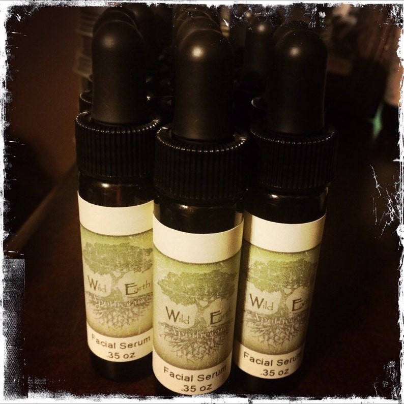 May include: A group of eight small, dark brown glass bottles with black caps and white labels. The labels have a green tree design and the text "Wild Earth Facial Serum 35 oz".