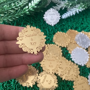 May include: Gold mirror acrylic wedding favours with a decorative design and the names "Natalia & Key" engraved on them.