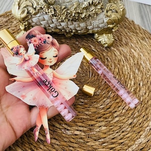 May include: Two perfume bottles with gold caps and pink liquid. One bottle is held by a fairy-shaped cutout. The fairy is wearing a pink dress and has a floral crown. The text "Gökçe" is printed on the bottle.