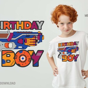 May include: A white t-shirt with a colorful graphic design featuring a toy gun and the words "Birthday Boy".