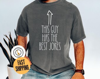 May include: A dark gray t-shirt with a white arrow pointing upwards and the text "This guy has the best jokes".