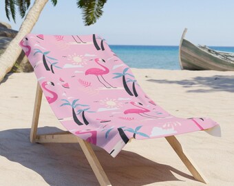 Op de afbeelding: Een roze strandstoel met een flamingo-patroon. Het ontwerp omvat roze flamingo's, palmbomen, zonnen en wolken. De stoel is gemaakt van hout en stof, geplaatst op een zandstrand met uitzicht op de oceaan en een boot.