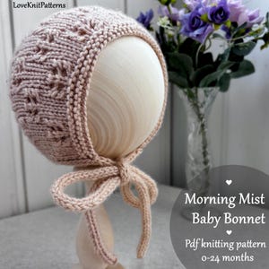 May include: A light brown knitted baby bonnet with a textured pattern and a bow tie. The bonnet is displayed on a wooden head form. The text on the image says "Morning Mist Baby Bonnet" and "Pdf knitting pattern 0-24 months".