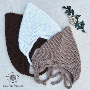 May include: Three pointed bonnets in dark brown, white, and light brown, each featuring a textured knit pattern and chin ties. The bonnets are arranged in a layered stack, with the dark brown one at the bottom, white in the middle, and light brown on top.