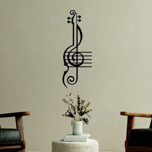 Pu&ograve; includere: Arte da parete in metallo nero con una chiave di violino e un violino stilizzato. L'arte &egrave; montata su una parete beige chiaro con un vaso di fiori secchi e una sedia di legno su entrambi i lati.