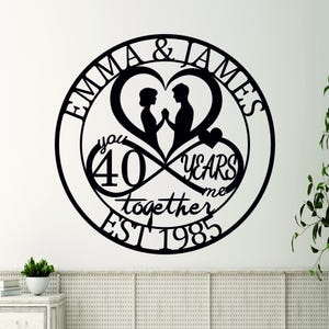 May include: Black metal wall art with an infinity symbol design. The symbol features two hearts with a couple inside, the text "Emma & James", "You 40 Years Me Together Est 1985", and a small heart.
