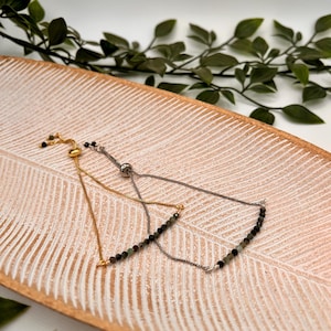 Puede incluir: Dos pulseras ajustables con una cadena dorada y plateada y una fila de cuentas negras y verdes.