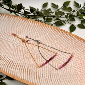 May include: Three adjustable bracelets with pink gemstone beads and silver and gold chains. The bracelets are displayed on a wooden tray.