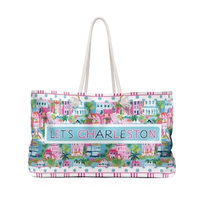 May include: A large tote bag with white rope handles. The bag features a colorful pattern of Charleston houses, palm trees, and the text "LET'S CHARLESTON" on a light blue background. The bag has a white and pink polka dot border.