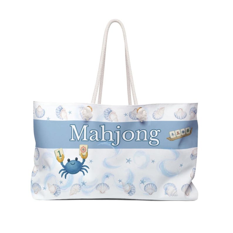 May include: White tote bag with a blue stripe featuring the word "Mahjong". The bag has a seashell and crab design. It has white rope handles.