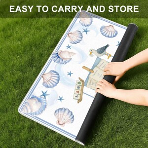 May include: A rolled-up white mat with a blue border, featuring seashell and starfish illustrations. The mat has the text "EASY TO CARRY AND STORE" at the top. The mat is being rolled up by a person.