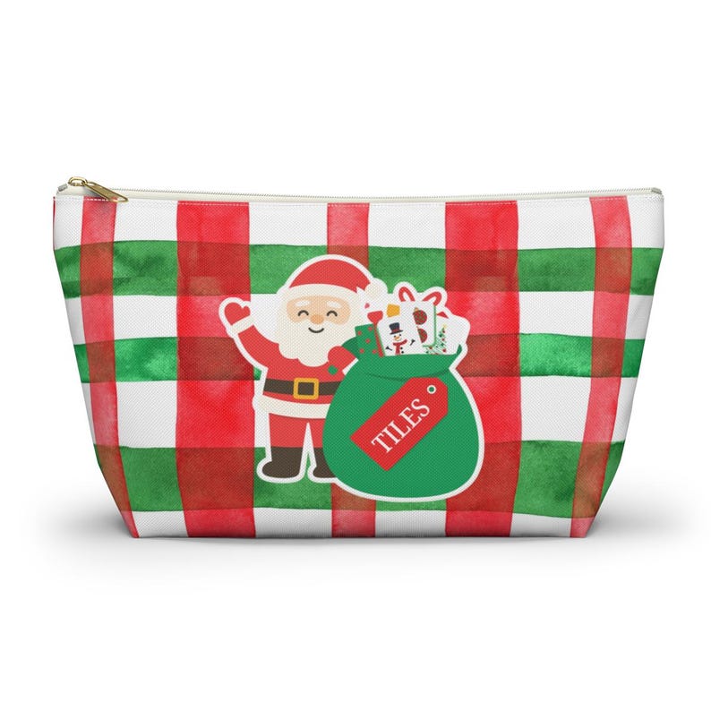 May include: A zippered pouch with a red, green, and white plaid pattern. A Santa Claus graphic is on the front, holding a green bag labeled "TILES" filled with gifts. The pouch is designed for carrying items.