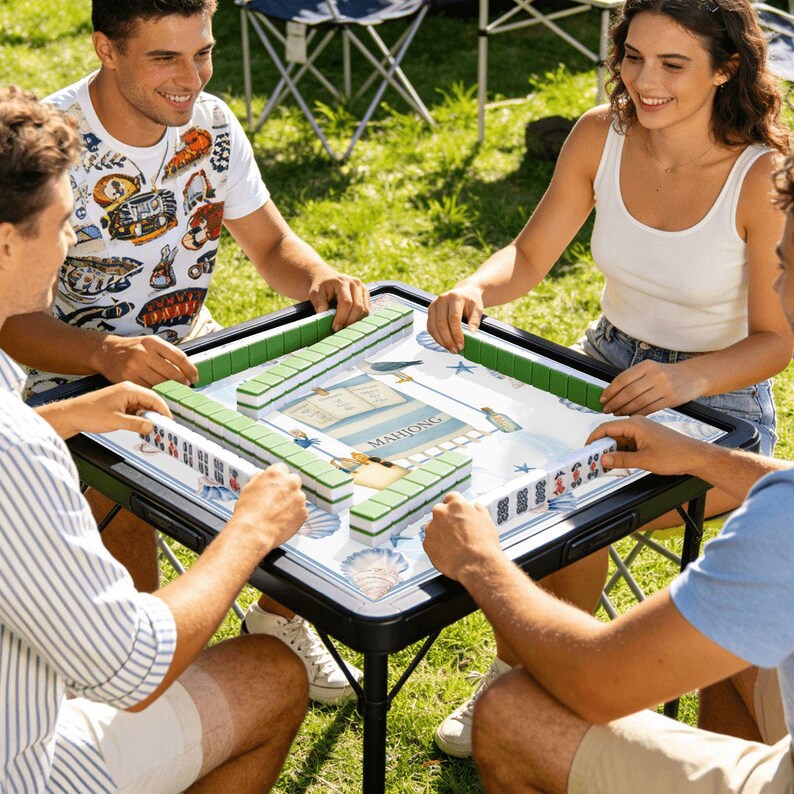 May include: A group of four people playing Mahjong outdoors. The game is set up on a black folding table with a patterned playing surface. Green and white tiles are arranged around the table. The players are smiling and interacting with each other.