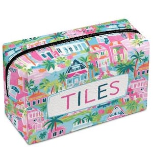 May include: Rectangular cosmetic bag with a colorful tropical print featuring houses, palm trees, and the word "TILES" in pink. The bag has a black zipper and a white label with pink lettering.