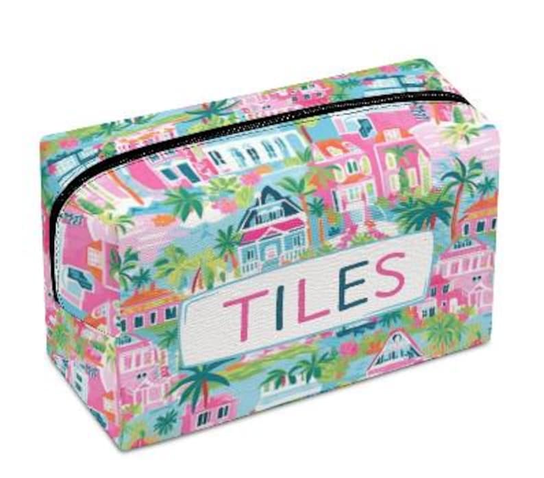May include: Rectangular cosmetic bag with a colorful tropical print featuring houses, palm trees, and the word "TILES" in pink. The bag has a black zipper and a white label with pink lettering.