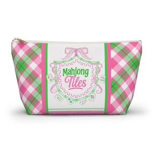 Può includere: Un astuccio con cerniera con un motivo a quadri rosa, verde e bianco. Il centro presenta la scritta "Mahjong Tiles" in verde e rosa, circondata da una cornice decorativa e un fiocco rosa.