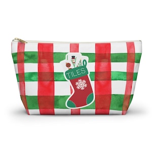 May include: A zippered pouch with a red, green, and white plaid pattern. A Christmas stocking graphic is on the front, filled with gifts and the word "TILES". The stocking is red with a green cuff and a white snowflake.