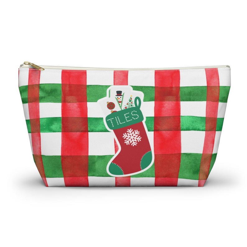 May include: A zippered pouch with a red, green, and white plaid pattern. A Christmas stocking graphic is on the front, filled with gifts and the word "TILES". The stocking is red with a green cuff and a white snowflake.