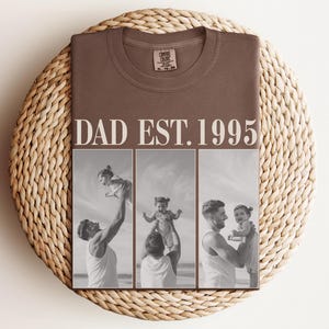 Folded espresso brown t-shirt with bold ivory “DAD EST. 1995” text and a three-photo black-and-white collage of a dad and daughter sharing joyful moments at the beach. Displayed on a round woven mat in a warm flat lay scene. Perfect custom gift for Father’s Day, new dads, or dad’s birthday. Unisex Comfort Colors tee with heartfelt design and personalized photo print.