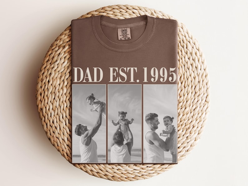 Folded espresso brown t-shirt with bold ivory “DAD EST. 1995” text and a three-photo black-and-white collage of a dad and daughter sharing joyful moments at the beach. Displayed on a round woven mat in a warm flat lay scene. Perfect custom gift for Father’s Day, new dads, or dad’s birthday. Unisex Comfort Colors tee with heartfelt design and personalized photo print.