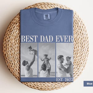 Folded blue jean Comfort Colors t-shirt with bold “BEST DAD EVER” text and a black-and-white three-photo collage of a dad lifting and cuddling his child, with “EST. 2023” at the bottom. Displayed on a woven mat in a cozy flat lay. Personalized photo shirt perfect for new dads, Father’s Day, or baby’s first birthday. A thoughtful and stylish keepsake tee celebrating fatherhood.