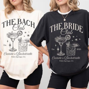 May include: Two black and white t-shirts with a cocktail glass graphic and text that reads "The Bach Club" and "The Bride Club". The text also includes "Camila's Bachelorette" and "Palm Springs, CA".