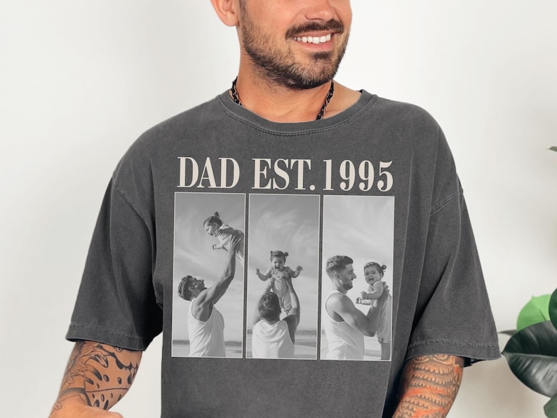 Charcoal unisex t-shirt featuring bold text “DAD EST. 1995” above a custom three-photo collage of a father and daughter. Black-and-white beach images showcase heartfelt moments of fatherhood. Perfect personalized Father’s Day gift, birthday present, or first-time dad keepsake. Oversized fit with a vintage look—ideal for sentimental, stylish, and custom apparel lovers.