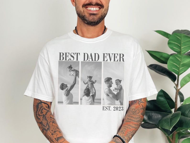 White Comfort Colors t-shirt worn by a smiling man, featuring bold “BEST DAD EVER” text and a black-and-white three-photo collage of a dad with his child, with “EST. 2023” at the bottom. Personalized gift perfect for new dads, Father’s Day, or baby’s first birthday. A sentimental and stylish custom photo shirt to celebrate fatherhood and cherished memories.