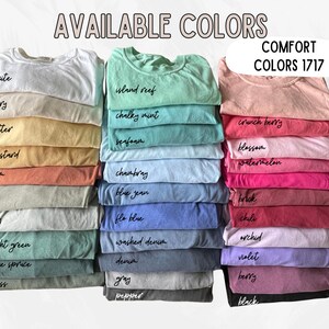 May include: A variety of t-shirt colors, stacked and labeled with their names. The colors include white, ivory, butter, mustard, yarn, bay, light green, blue spruce, moss, island reef, chalky mint, seafoam, chambray, blue jean, flo blue, washed denim, denim, gray, pepper, crunch berry, blossom, watermelon, brick, chili, orchid, violet, berry, and black. The text "COMFORT COLORS 1717" is at the top of the image.
