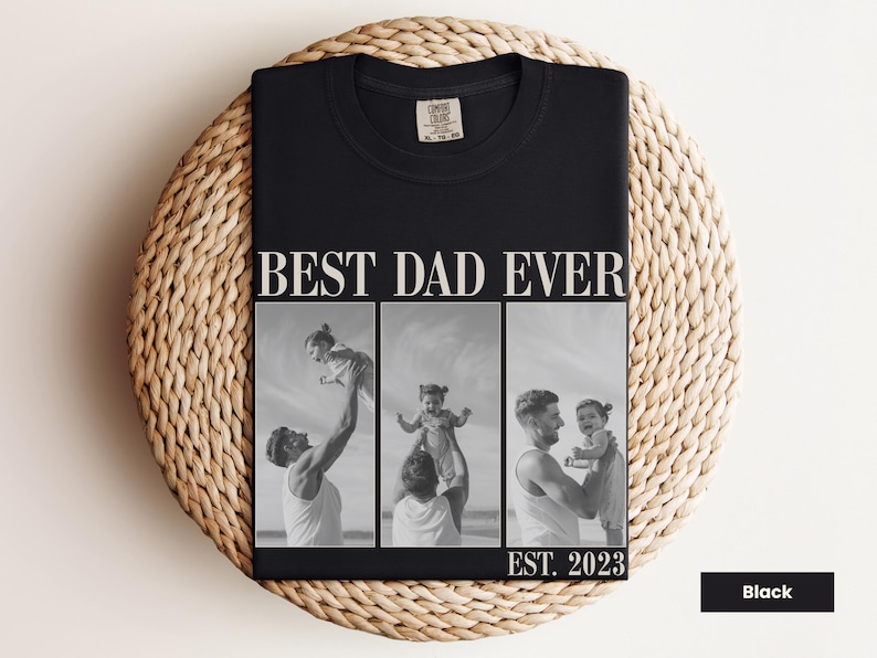 Folded black Comfort Colors t-shirt with bold “BEST DAD EVER” text and a black-and-white three-photo collage of a dad holding and playing with his baby, labeled “EST. 2023.” Displayed on a woven mat in a cozy flat lay. Personalized gift for first-time dads, Father’s Day, or baby’s first birthday. A heartfelt, custom keepsake shirt celebrating the joy of fatherhood.