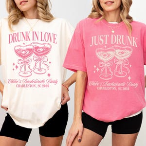 May include: Two t-shirts, one ivory and one pink, with matching graphic designs. The ivory shirt reads "DRUNK IN LOVE" and the pink shirt reads "JUST DRUNK". Both shirts feature a heart-shaped cocktail glass design and text that reads "Chloe's Bachelorette Party, Charleston, SC 2026".